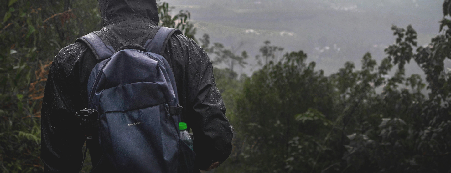Man wearing black rain jacket, facing forward with forest background.