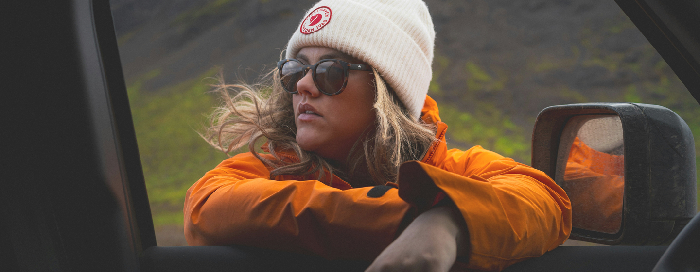 Woman wearing orange rain jacket leaning against a car window