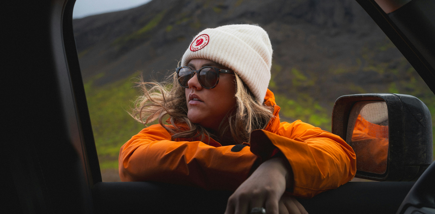 Woman wearing orange rain jacket leaning against a car window