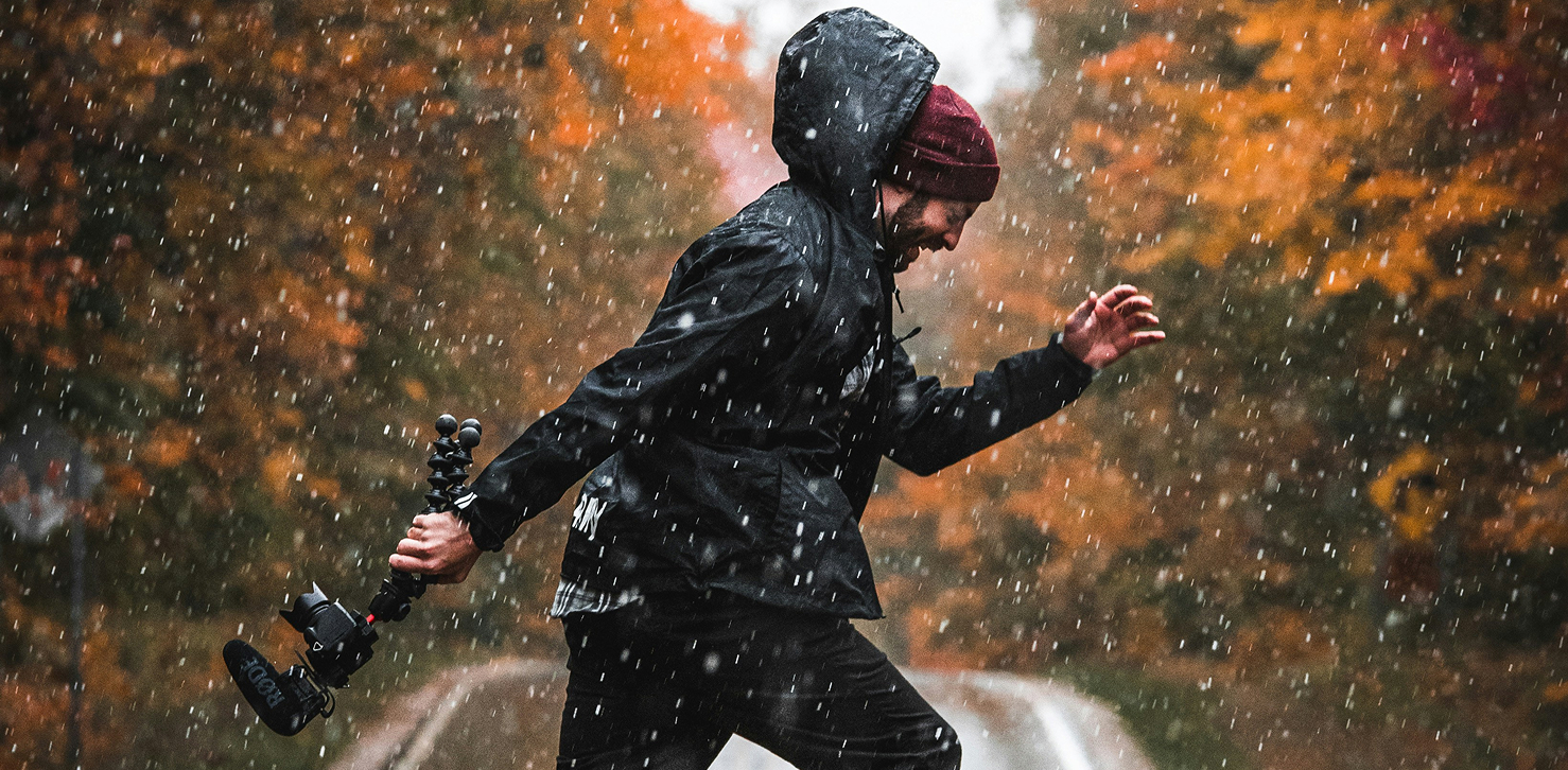 Man wearing black rain jacket while jumping in the rain with a forest background