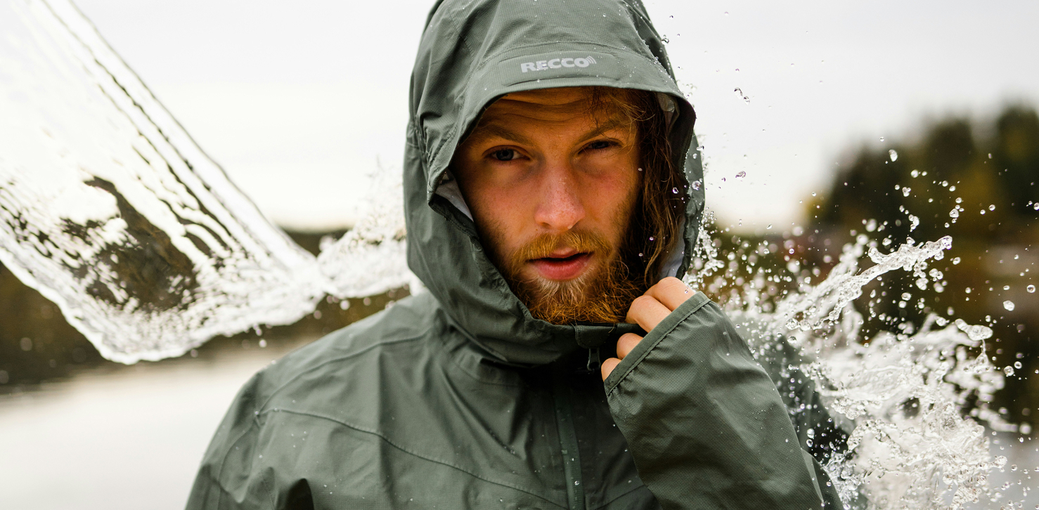 Man wearing green rain jacket while getting water splashed on him